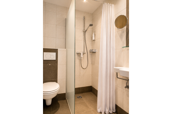 A modern bathroom with a shower and a white shower curtain. There is a toilet and a sink on the wall. - Gästehaus Fernblick - Sautens