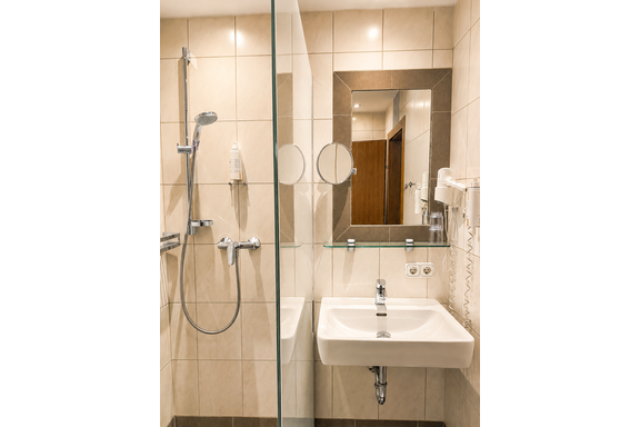 A modern bathroom with a shower and a sink. The walls are tiled in light colors, and there is a large mirror. - Gästehaus Fernblick - Sautens