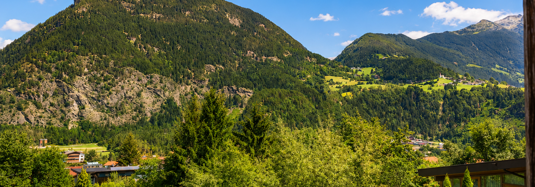 A picturesque mountain landscape with green forests and a clear blue sky. In the foreground, trees and a swimming pool are visible. - Gästehaus Fernblick - Sautens