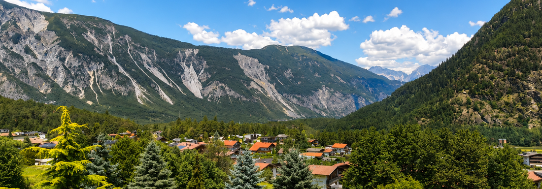 A picturesque mountain landscape with green forests and a clear blue sky. In the foreground, numerous trees and some remote houses are visible. - Gästehaus Fernblick - Sautens