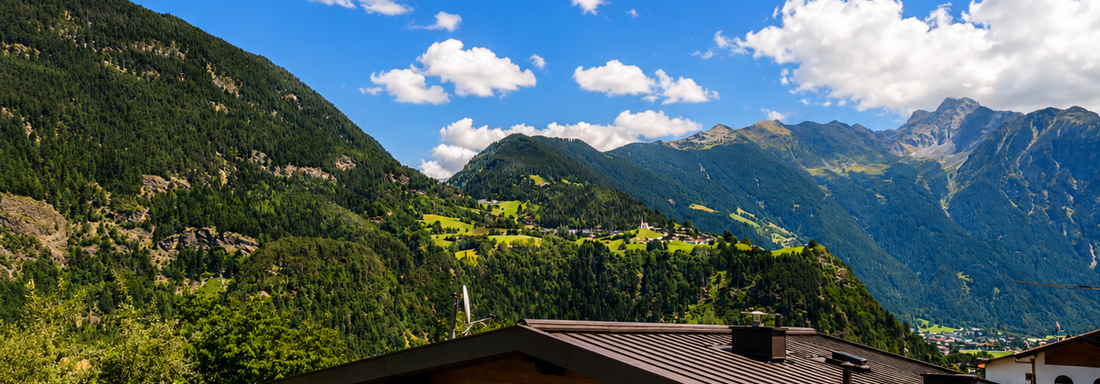 A picturesque mountain landscape with green hills and a bright blue sky. In the foreground, a cozy building can be seen. - Gästehaus Fernblick - Sautens