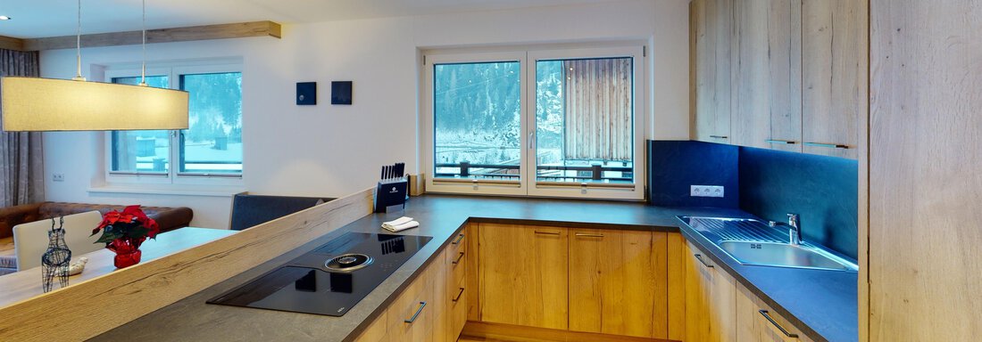 A modern kitchen with wooden cabinets and a simple countertop. Large windows provide plenty of natural light. - A CASA "Rubin Chalet & Studio Resort" - Sölden