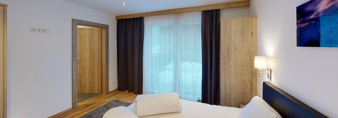 A modern bedroom with a large bed and bright wood details.  
Large windows let in plenty of light and provide access to a balcony. - A CASA "Rubin Chalet & Studio Resort" - Sölden