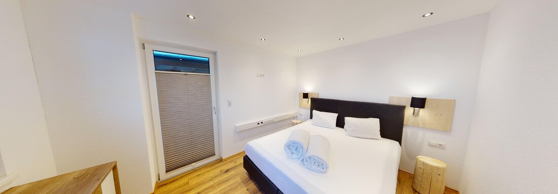 A modern bedroom with a large double bed and two pillows.  
Bright walls and wooden floors create a pleasant atmosphere. - A CASA "Rubin Chalet & Studio Resort" - Sölden