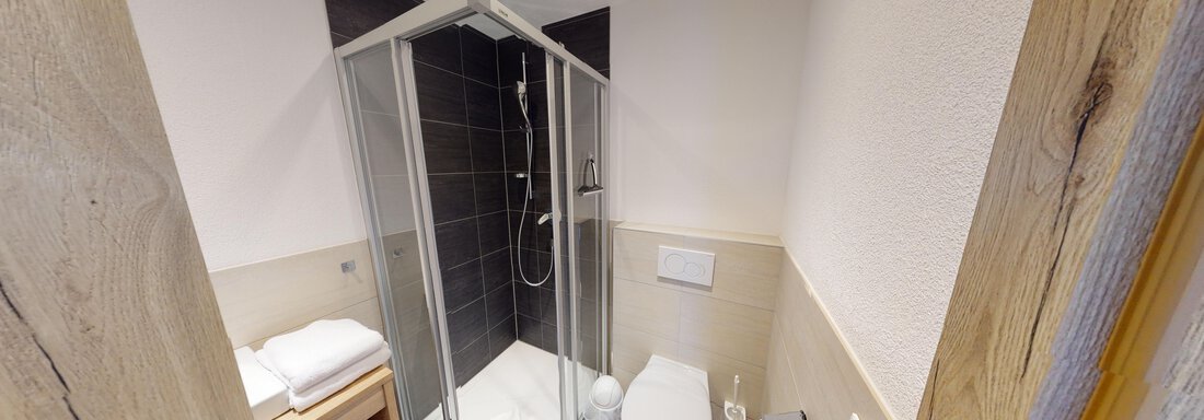 A modern bathroom with a shower, a toilet, and a wooden shelf. The room design is simple and functional. - A CASA "Rubin Chalet & Studio Resort" - Sölden