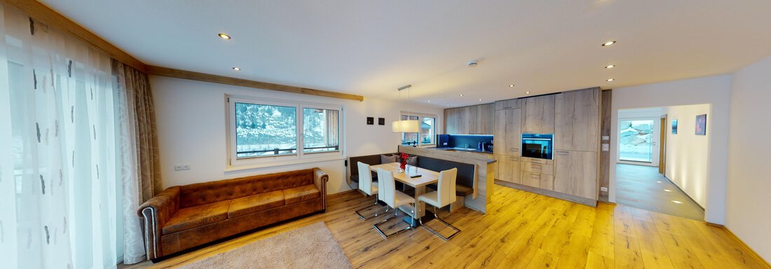 A modernly designed living room with wooden flooring and plenty of natural light. There is a cozy couch, a dining table, and an open kitchen in the background. - A CASA "Rubin Chalet & Studio Resort" - Sölden