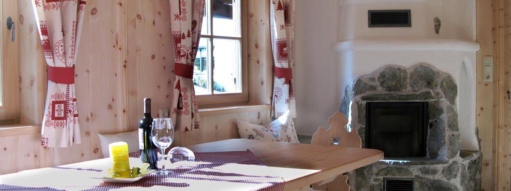 A cozy room with wooden walls and large windows. A dining table with chairs and a fireplace in the background creates an inviting atmosphere. - Almdorf Waldesruh - Sölden