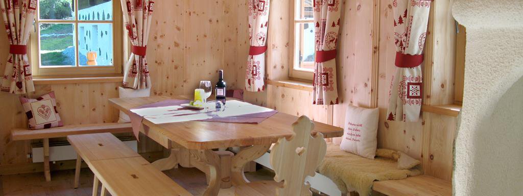 Zirmstube A cozy room with wood paneling and large windows. At the center is a wood-carved table with benches and a bottle of wine. - Almdorf Waldesruh - Sölden