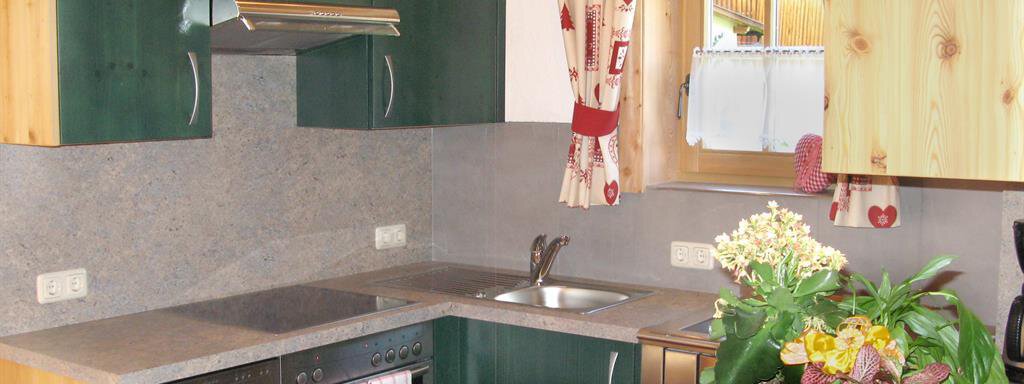 A modern kitchen with green cabinets and wood details. On the countertop, there is a bouquet of flowers in a basket. - Almdorf Waldesruh - Sölden
