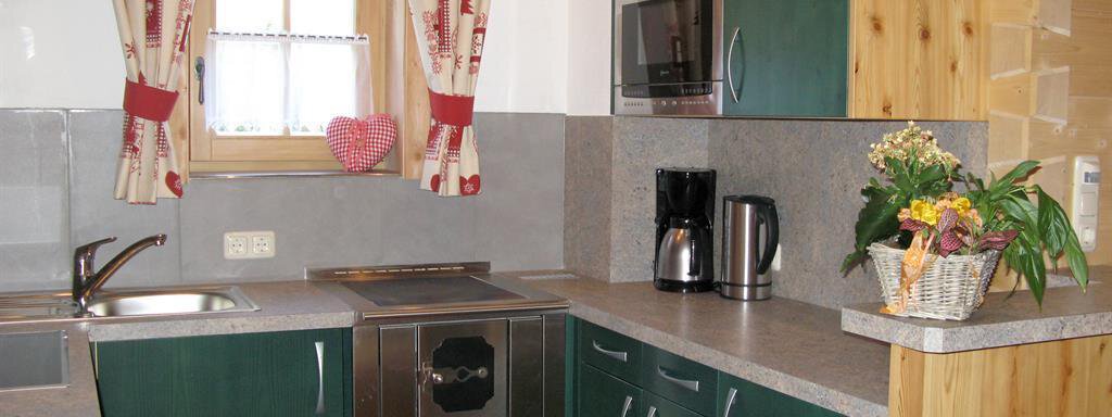 A cozy kitchen with green cabinets and modern appliances. The space features wood and stone accents as well as a windowsill with curtains. - Almdorf Waldesruh - Sölden