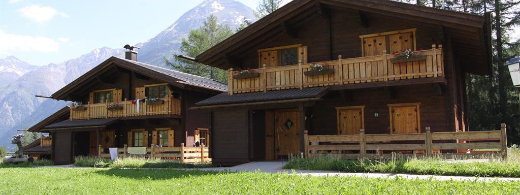 Two charming wooden houses in a picturesque mountain landscape. In the background, tall mountains and a clear sky can be seen. - Almdorf Waldesruh - Sölden