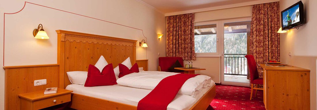 Doppelzimmer Standard A comfortable room with a large bed and red accents. The cozy atmosphere is enhanced by a television and a balcony. - Alp Resort Tiroler Adler - Sölden