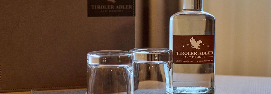 A bottle of water is on a table, accompanied by two glasses. In the background, a black menu is visible. - Alp Resort Tiroler Adler - Sölden