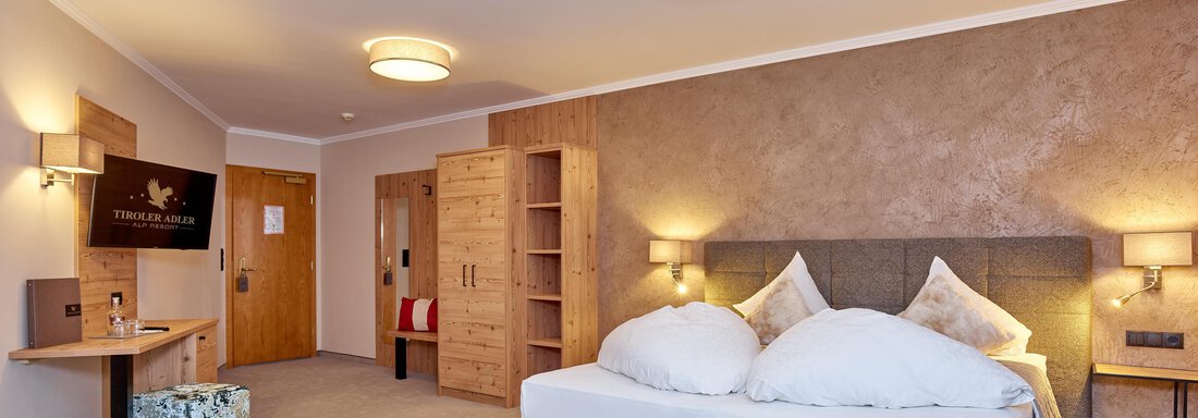 A modern hotel room with a large bed and cozy decor. There is a table, a television, and a wooden piece of furniture. - Alp Resort Tiroler Adler - Sölden