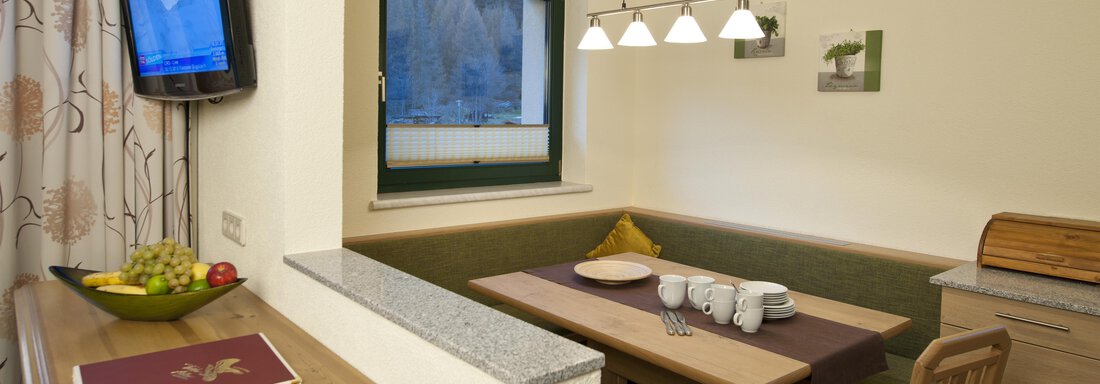 A cozy dining area with a wooden table and benches. A television is mounted on the wall, and there is a window with a view. - Alp Resort Tiroler Adler - Sölden