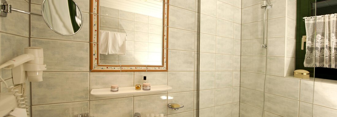 A modern bathroom with bright tiles and a bathtub. In the foreground, a sink, a mirror, and a hairdryer are visible. - Alp Resort Tiroler Adler - Sölden