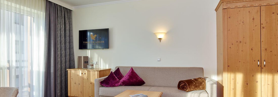A cozy living room with a bright sofa and a wooden table. The walls are painted in neutral colors, and a wooden cabinet stands in the room. - Alp Resort Tiroler Adler - Sölden