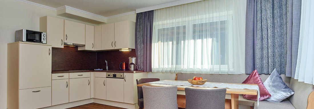 A modern kitchen with a dining table and chairs.  
Plenty of light streams through the large windows, and the decor is cozy and inviting. - Alp Resort Tiroler Adler - Sölden