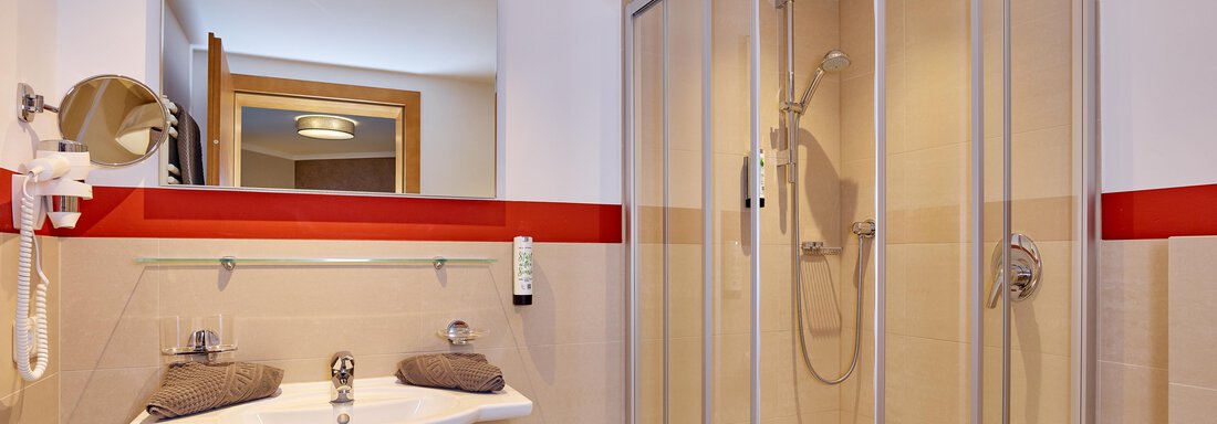 A modern bathroom with a glass shower and a sink. The walls are designed in light colors with red accents. - Alp Resort Tiroler Adler - Sölden
