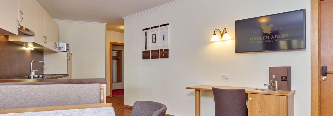 A modern room with a kitchenette and a desk. The wooden floors and warm colors create a cozy atmosphere. - Alp Resort Tiroler Adler - Sölden