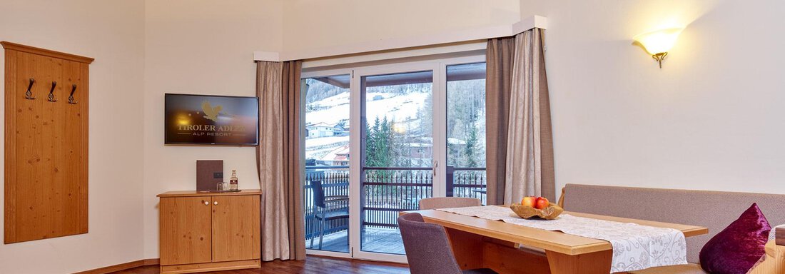 A cozy living area with wooden flooring and a wooden ceiling. There is a dining area, a television, and large windows with a view of the balcony. - Alp Resort Tiroler Adler - Sölden