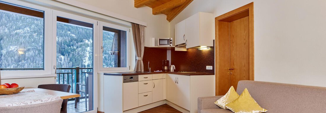 A cozy living environment with wooden beam ceiling and large windows. The modern kitchen and dining area offer an inviting atmosphere. - Alp Resort Tiroler Adler - Sölden