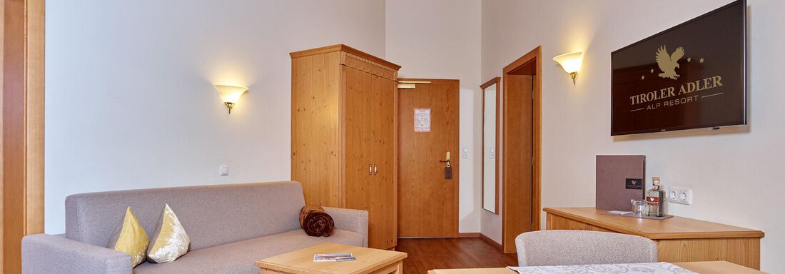 An inviting living environment with a wooden ceiling and bright walls. The room is furnished with a sofa, a table, and a TV. - Alp Resort Tiroler Adler - Sölden
