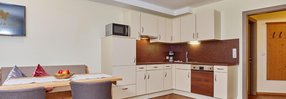 A modern kitchen with dining table and chairs. The walls are painted light and the floor is made of wood. - Alp Resort Tiroler Adler - Sölden