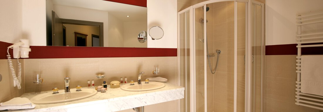 A modern bathroom with two sinks and a shower booth. The walls are designed in neutral colors with red accents. - Alp Resort Tiroler Adler - Sölden