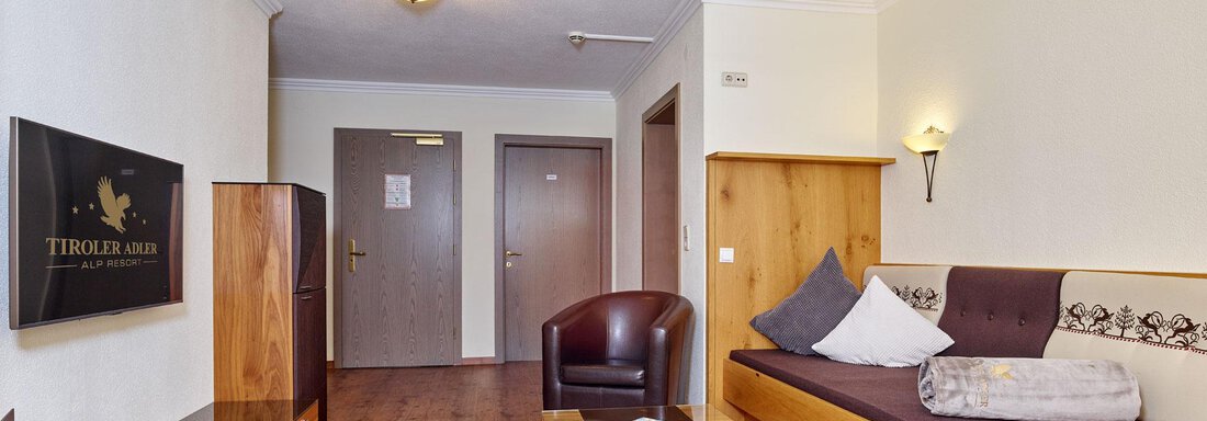 A modern living room with a sofa, an armchair, and a coffee table. The space is bright and offers access to additional doors. - Alp Resort Tiroler Adler - Sölden