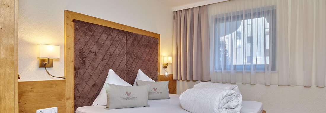 A cozy bedroom with a wooden bed and a large window. The walls are painted in soft colors, and there are light curtains. - Alp Resort Tiroler Adler - Sölden
