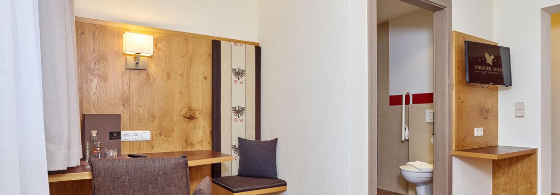 A simple hotel room with a desk and a chair. The bathroom is visible and modernly furnished. - Alp Resort Tiroler Adler - Sölden