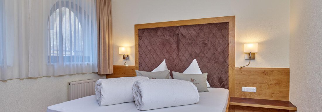 A cozy bedroom with a large wooden bed and white pillows. The soft lighting creates a relaxed atmosphere. - Alp Resort Tiroler Adler - Sölden