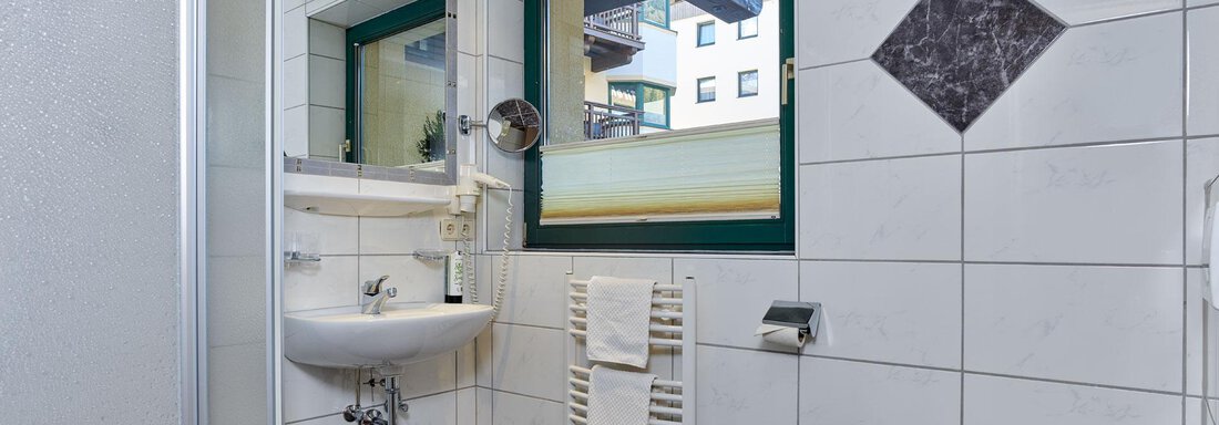 A bright bathroom with white tiles and a large window. It is modernly furnished with a sink, shower, and toilet. - Alp Resort Tiroler Adler - Sölden