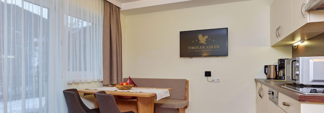 A modern kitchen with a dining area and wooden flooring. The large windows let in plenty of light and create an inviting atmosphere. - Alp Resort Tiroler Adler - Sölden