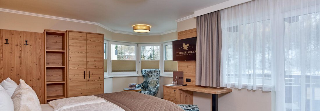 CF056520-2 A modern room with a cozy bed and warm wooden furniture. Large windows let in natural light and offer a view outside. - Alp Resort Tiroler Adler - Sölden