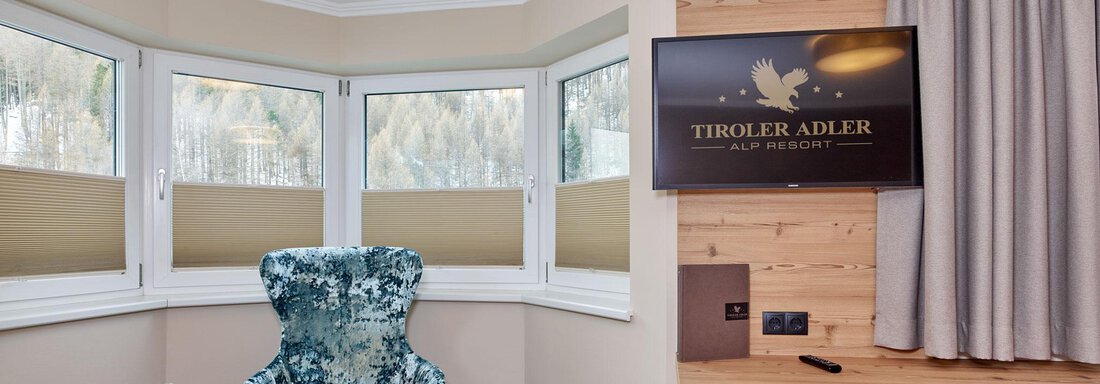 A cozy lounge area with a blue armchair and a small table. A television and a wooden dresser complement the modern design. - Alp Resort Tiroler Adler - Sölden