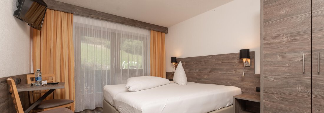 Zimmerfotos-1 A modern hotel room with a large double bed and a television. Curtains and wooden furniture create a cozy atmosphere. - Alpenliebe - Sölden