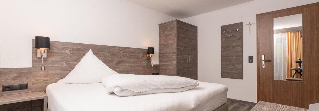 A modern bedroom with a large bed and wooden interior. The walls are bright and the lighting creates an inviting atmosphere. - Alpenliebe - Sölden