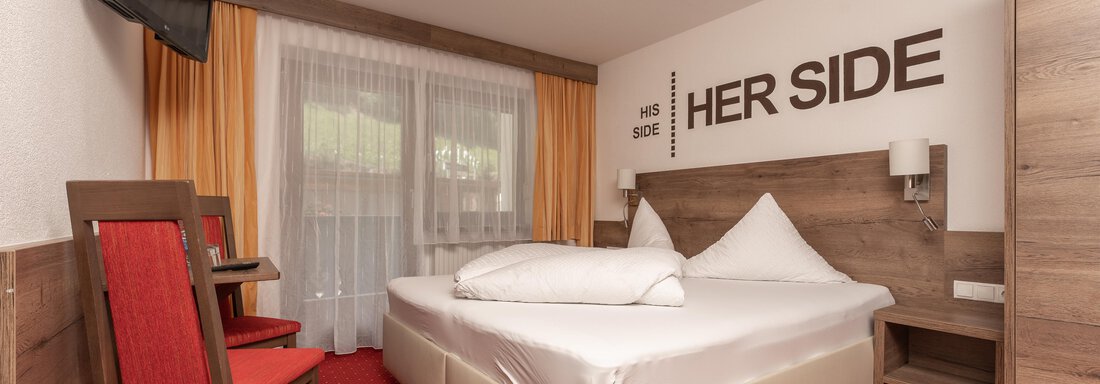A cozy bedroom with a double bed and a red carpet. On the wall is the inscription "HER SIDE" and the window lets in plenty of daylight. - Alpenliebe - Sölden