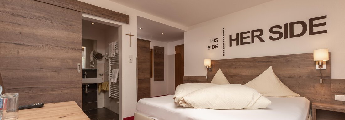 A modern bedroom with a large double bed and a cozy atmosphere. The walls display the words "HIS SIDE" and "HER SIDE". - Alpenliebe - Sölden