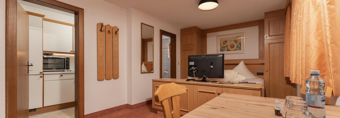 A cozy room with wooden details and a desk. In the background, a kitchen is visible and the light is warm and inviting. - Alpenliebe - Sölden