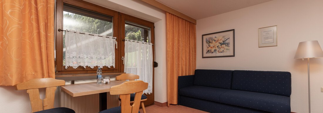 A cozy living space with a blue sofa and a table with two chairs. Large windows provide plenty of daylight and a friendly atmosphere. - Alpenliebe - Sölden