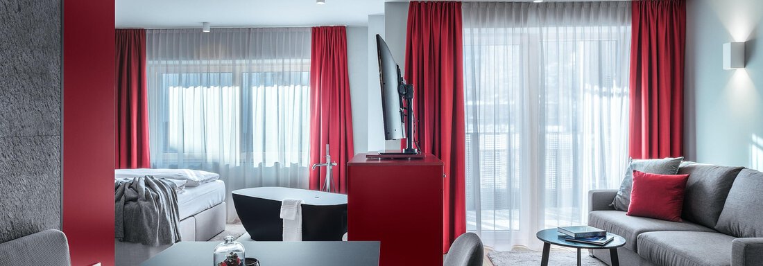 A modern apartment with red curtains and a cozy living area. The space is bright and inviting, with a dining area and a large window front. - AlpenParks The Secret Sölden - Sölden