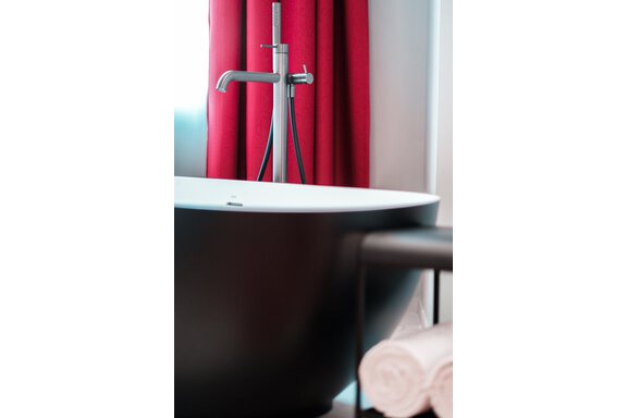 An elegant bathroom with a modern black bathtub and a stylish faucet. In the background, red curtains and fresh towels are visible. - AlpenParks The Secret Sölden - Sölden