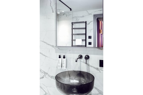A modern bathroom with an elegant black wash basin. The walls are designed with a marbled pattern and a large mirror reflects the surroundings. - AlpenParks The Secret Sölden - Sölden