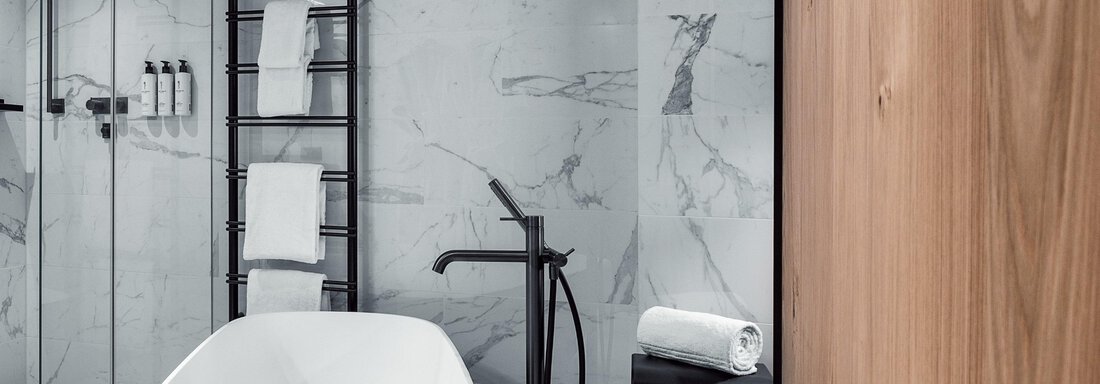 A modern bathroom with an elegant freestanding bathtub and a modern shower. The walls are adorned with stylish marble. - AlpenParks The Secret Sölden - Sölden