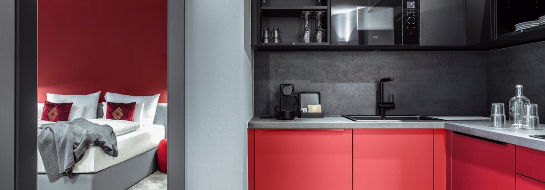 Modern kitchen with red cabinets and black work area. In the background, a stylish bedroom can be seen. - AlpenParks The Secret Sölden - Sölden