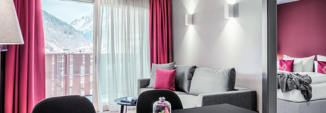 A modern living room with a large window and a beautiful view of the mountains. The decor is elegant with red curtains and cozy furniture. - AlpenParks The Secret Sölden - Sölden