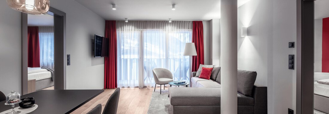 A modern living and dining room with an elegant sofa and a table. Large windows provide plenty of daylight and a bright, inviting atmosphere. - AlpenParks The Secret Sölden - Sölden